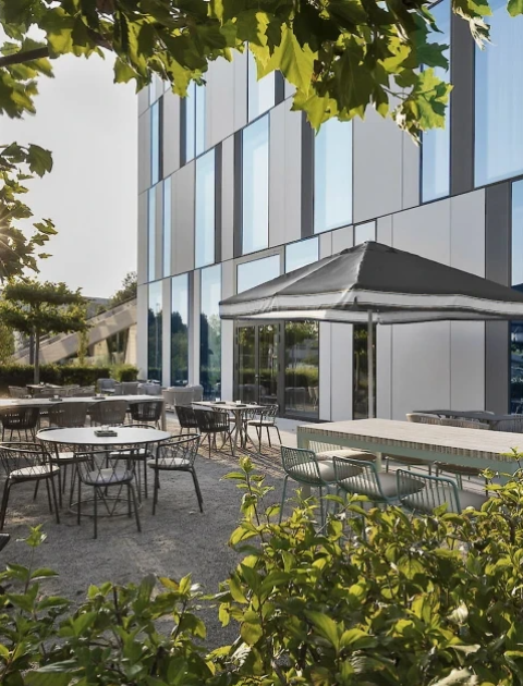 Moderne Außenterrasse mit Tischen vor Hotelfassade im Sommerlicht